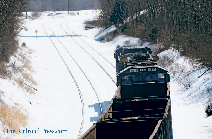CSX iron ore train rolling through the snow and heading away from you as it rolls beneath the Grade Road bridge at Martinsburg, West Virginia, on February 14, 2014